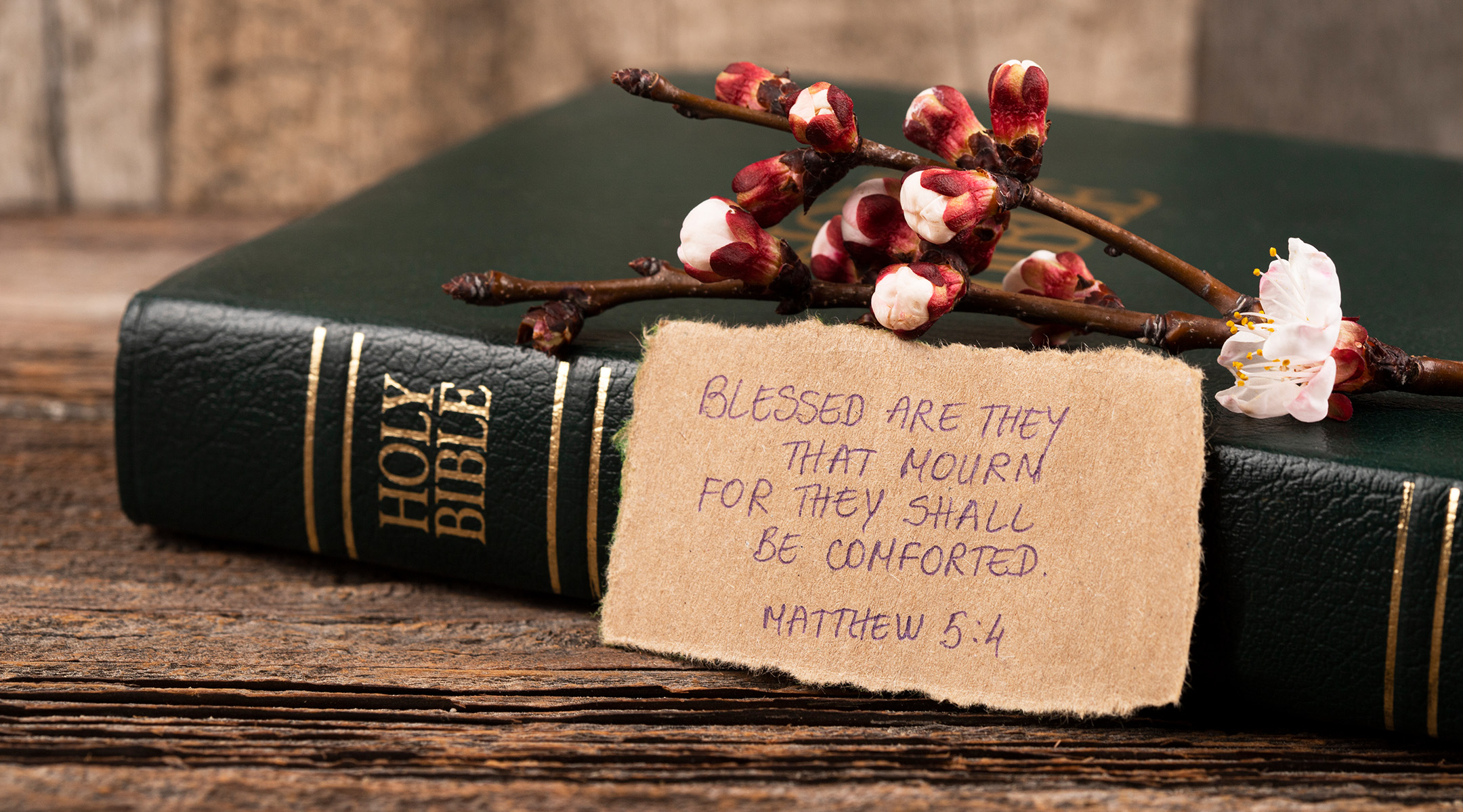 Single candle burning softly on a dark table beside an open Bible